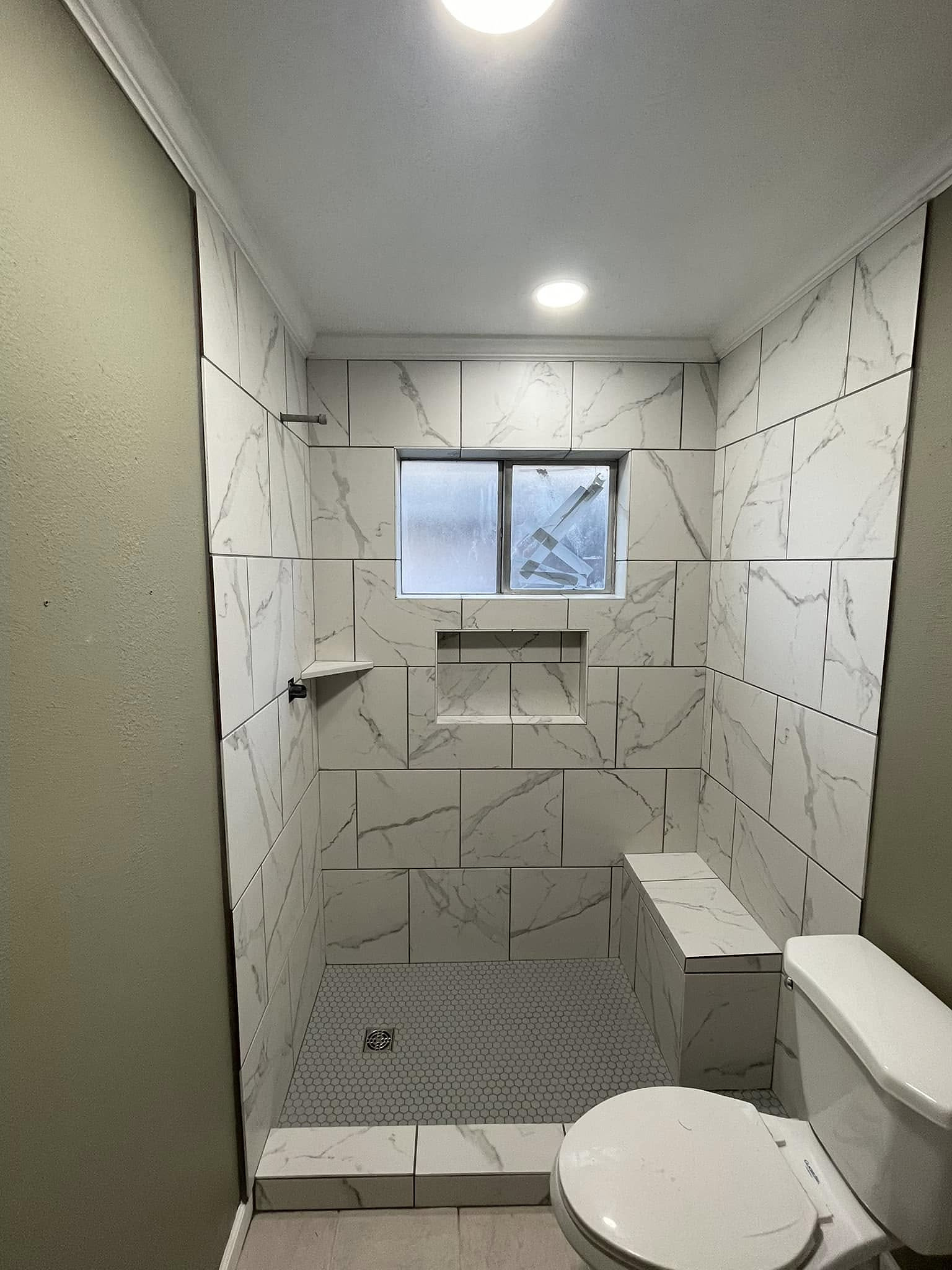 The same shower finished in white marble-look tile with bench and niche by Reeder