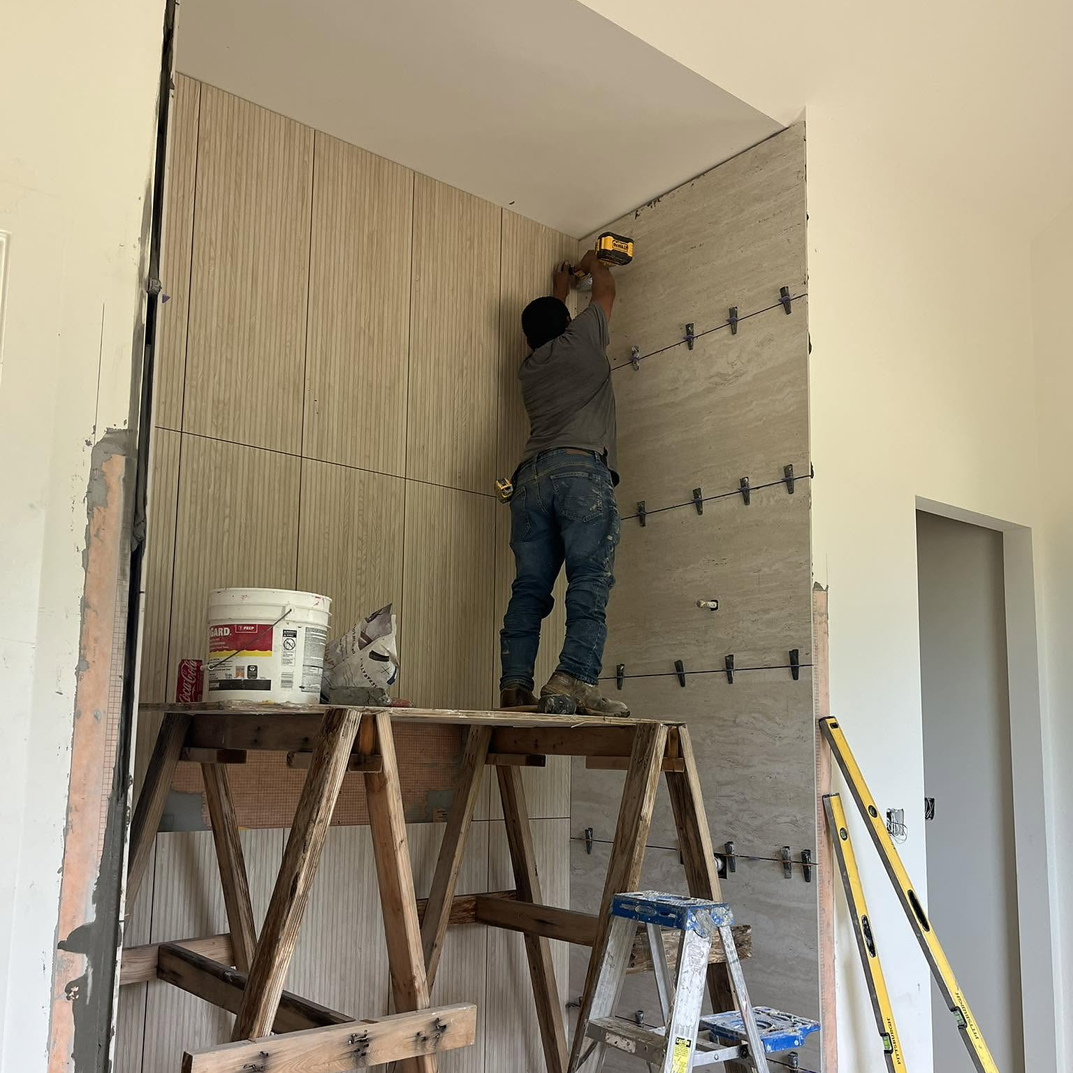 Reeder installer setting a travertine slab wall beside white oak paneling