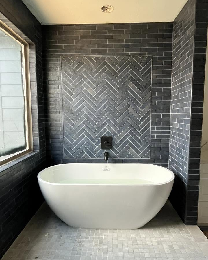 Freestanding tub against a charcoal herringbone tile feature wall by Reeder